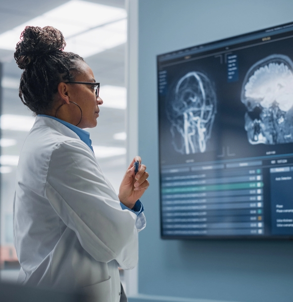 a person wearing a lab coat looking at a large monitor that shows images of a brain scan